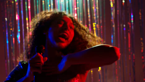 Young-Woman-With-Microphone-Singing-At-Karaoke-Nightclub-Bar-Or-Disco-With-Sparkling-Lights-In-Background-5